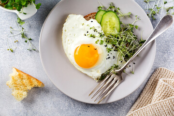 Fried eggs with arugula microgreen in gray ceramic plate on gray concrete old background....
