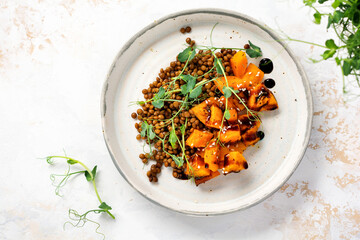 Salad with baked pumpkin, lentils and balsamic dressing garnished with peas microgreens on a light background. Healthy vegan food, top view