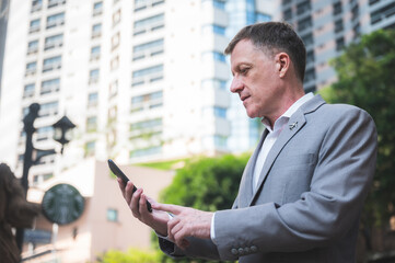 Fototapeta premium handsome executive manager businessman in suit using touch smart mobile phone to work on cyberspace, confident and successful with cellphone online message, walking in the city