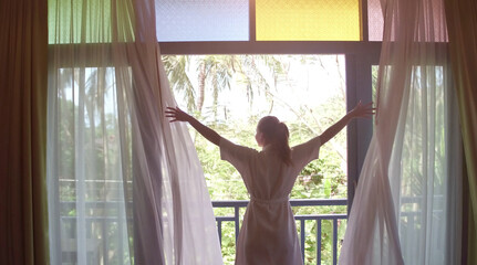  Lovely woman opening colorful curtains and meeting sunrise. View from balcony to jungle.