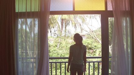  Lovely woman opening colorful curtains and meeting sunrise. View from balcony to jungle.