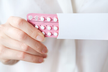 Unrecognized woman in white blouse holding hormonal oral contraceptives in a pink blister. Concept of Hormonal methods of birth control. Estrogen and Progestin hormonal balance. - obrazy, fototapety, plakaty