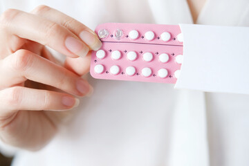 Unrecognized woman in white blouse holding hormonal oral contraceptives in a pink blister. Concept of Hormonal methods of birth control. Estrogen and Progestin hormonal balance. - obrazy, fototapety, plakaty