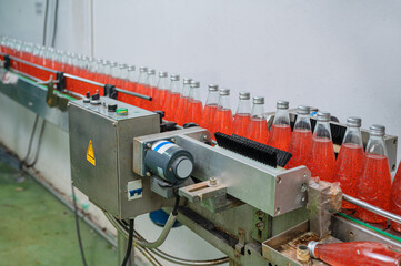 Glass bottled red juice on steel conveyor of production line in beverage processing factory