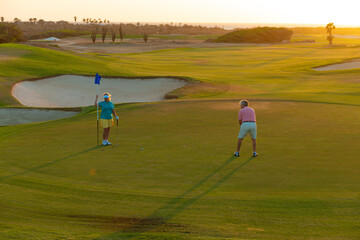 Active senior couple playing golf at sunset at the putting green.