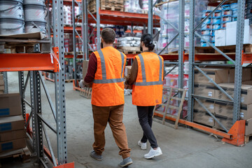 Two male workers with packed goods moving along racks