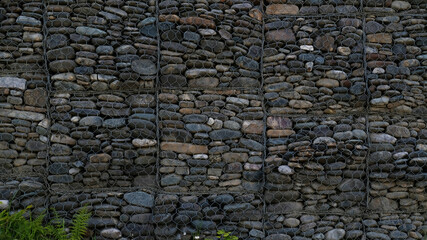 Gabion retaining wall - grey stones in gabion metallic baskets kept by retaining wall. Backdrop design and eco wall and die-cut for artwork. 