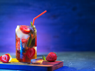 Refreshing summer strawberry mojito on a colored backlit blue background with copy space