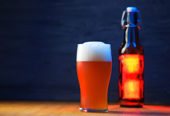 A tall glass of a pint of beer on a wooden table, a beer bottle with a bugle stopper. Unfiltered traditional wheat beer, copy space, blue backlight - obrazy, fototapety, plakaty