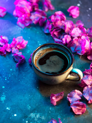 Obraz na płótnie Canvas Ceramic cup of black espresso coffee on a neon background with purple bougainvillea flowers