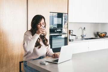 Woman working on laptop in kitchen at home