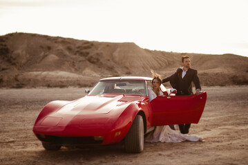 Newlyweds near red car in desert