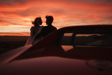 Loving couple resting near car at sunset