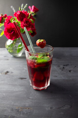 Cocktail with red wine, ice, strawberry, mint in high glass with straw on black background and rose flowers bouquet
