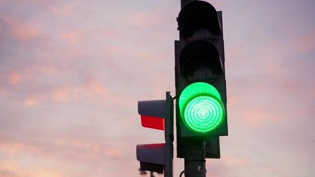 Cinematic hand-held shot. Close-up of a green traffic signal against the sunset sky.