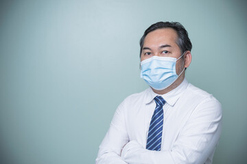 Fototapeta na wymiar Asian businessman wearing white shirt with blue tie and wearing a medical nose mask, standing with arms crossed. Looking at the camera with copy space. Business, Social distances, new normal concept.