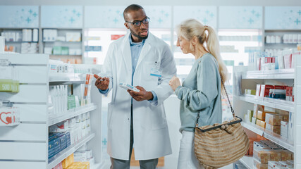 Obraz premium Pharmacy: Professional Black Helpful Pharmacist Advising Caucasian Senior Female Customer with Medicine Recommendation, Talking. Cusotmer Support in Drugstore Full of Drugs, Pill, Health Care Products