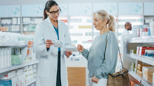 Pharmacy: Professional Pharmacist Helping Beautiful Senior Female Customer with Medicine Recommendation, Advice, Talking. Drugstore with Full of Drugs, Pills, Health Care, Beauty Product Packages