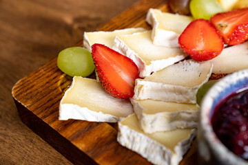 cheese assorted with fruit on wooden board.