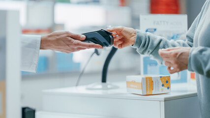 Obraz na płótnie Canvas Pharmacy Drugstore Checkout Cashier Counter: Pharmacist and a Customer Using Contactless Credit Card with Payment Terminal to Buy Prescription Medicine, Health Care Goods. Close-up Focus on Hands