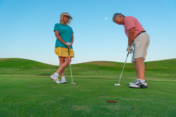 Active senior couple playing golf at sunset at the putting green.