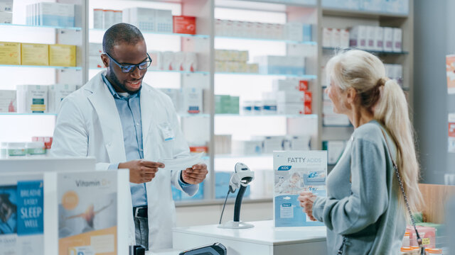 Pharmacy Drugstore Checkout Counter: Black Male Pharmacist Explains Use And Manual For Prescription Medicine Beautiful, Senior Female Customer Paying Using Contactless Credit Card To Terminal