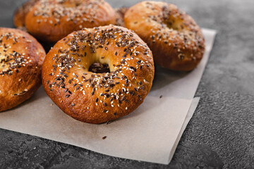 Close-up appetizing and crunchy bagels with sesame and flax seeds. Homemade hot baked goods. Bagels on baking paper on a gray concrete background. Cook at home. Copy space.