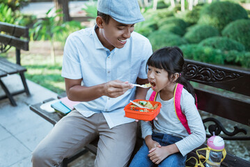 lovely father feed his daughter in the park before going to school in the morning