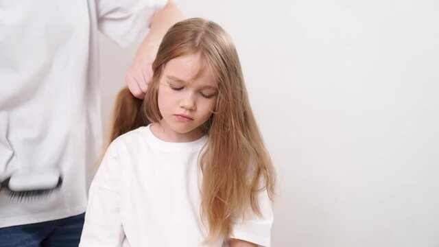 Mom combs her daughter's long blonde tangled hair. on a white background. care and cosmetics for children's hair.