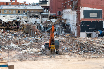 A crawler excavator with a special manipulator in front of a pile of debris from a destroyed...