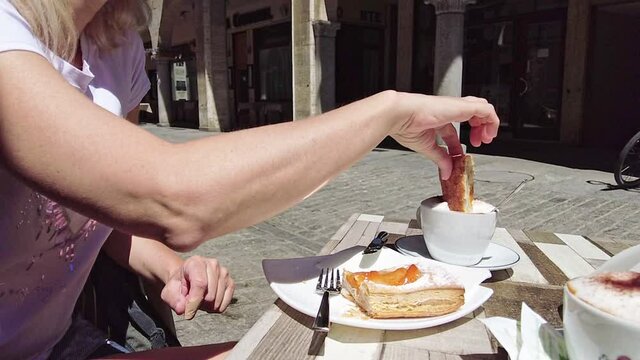 breakfast with cream pastry dipped in cappuccino in a coffee shop. close up of cake with marmalade. Bellinzona city in Switzerland.