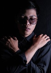 Studio portrait of a Thai Asian LGBT, woman handsomes beautiful hug yourself on a black backdrop. She's in a black shirt with Sad feelings.