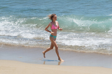 Healthy attractive woman wearing pink bikini running on the tropical beach against ocean. Sunshine summer day.