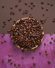 Coffee Beans in a Round Wooden Bowl and Scattered around on a Purple and Brown Background