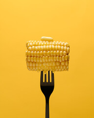 Corn cob on fork and melting dripping butter on a yellow background. 