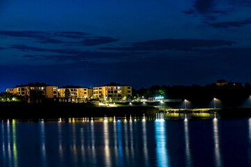 Naklejka premium Cottages and villas in the night city with light reflection in the water. Night city on the waterfront.