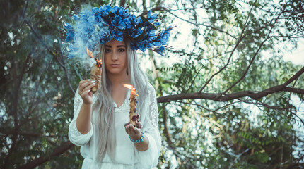 Beautiful girl in wreath of flowers in forest. Portrait of Young beautiful woman wearing white bride dress. Young pagan Slavic girl conduct ceremony on Midsummer. Earth Day