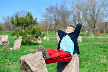 Naklejka na ściany i meble The boy is resting lying on the stones and enjoying the sun and silence.