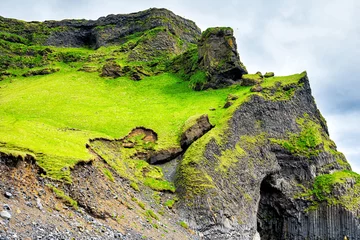 Fototapeten Lindgrün Icelandic green meadow field grass hill mountain rocky cliff landscape in Iceland summer in Reynisfjara, Vik with basalt cave  © Andriy Blokhin