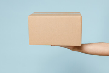 Close up cropped employee courier male hold in hand brown clear blank paper empty cardboard box isolated on blue color background Packaging mockup Delivery service concept Copy space Advertising area
