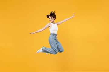 Full length young fun happy overjoyed woman 20s with bob haircut wearing white tank top shirt jumping high with outstretched hands like flying isolated on yellow background People lifestyle concept