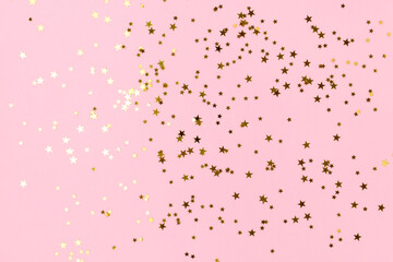 Shiny gold colored glittering stars confetti on a pink pastel background.