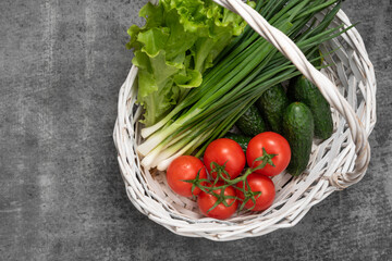 vegetables in a basket on a dark stone background. lettuse, scallion, cucumbers and tomatoes