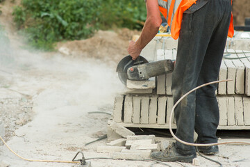 a worker in overalls cuts off a piece of concrete curb using an electric grinder, close-up