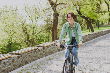 Young satisfied smiling happy woman 20s wear casual green jacket jeans riding bicycle bike on...