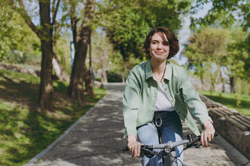 Young pensive dreamful happy woman 20s wearing casual green jacket jeans riding bicycle bike on...