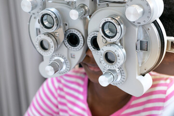Dark skinned girl looking through optical Phoropter during eye exam, diagnostic ophthalmology equipment, selective focus
