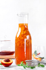 Bottle of iced tea with nectarine, peach and lemon on the white table. Making refreshing summer drink