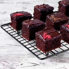 Brownie cakes with ganache and assorted toppings on the cooling rack on the white table