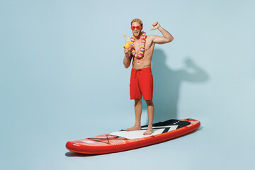 Full length young man in red shorts swimsuit hawaii lei glasses stand sup board hold alcohol...